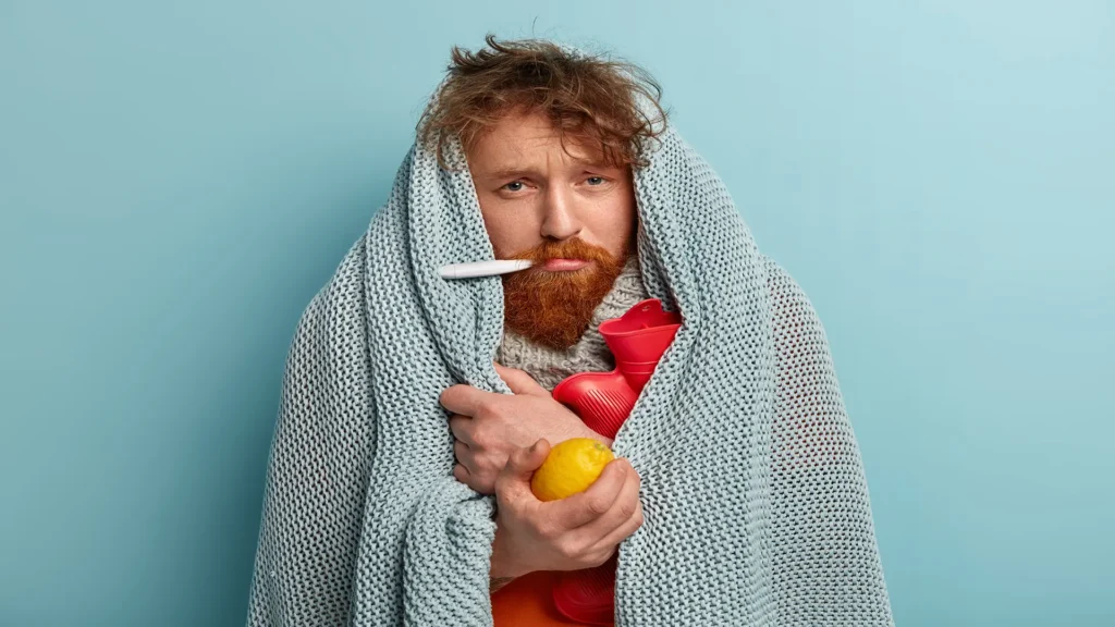 sick man warm clothes with thermometer holds lemon hot water bottle copy